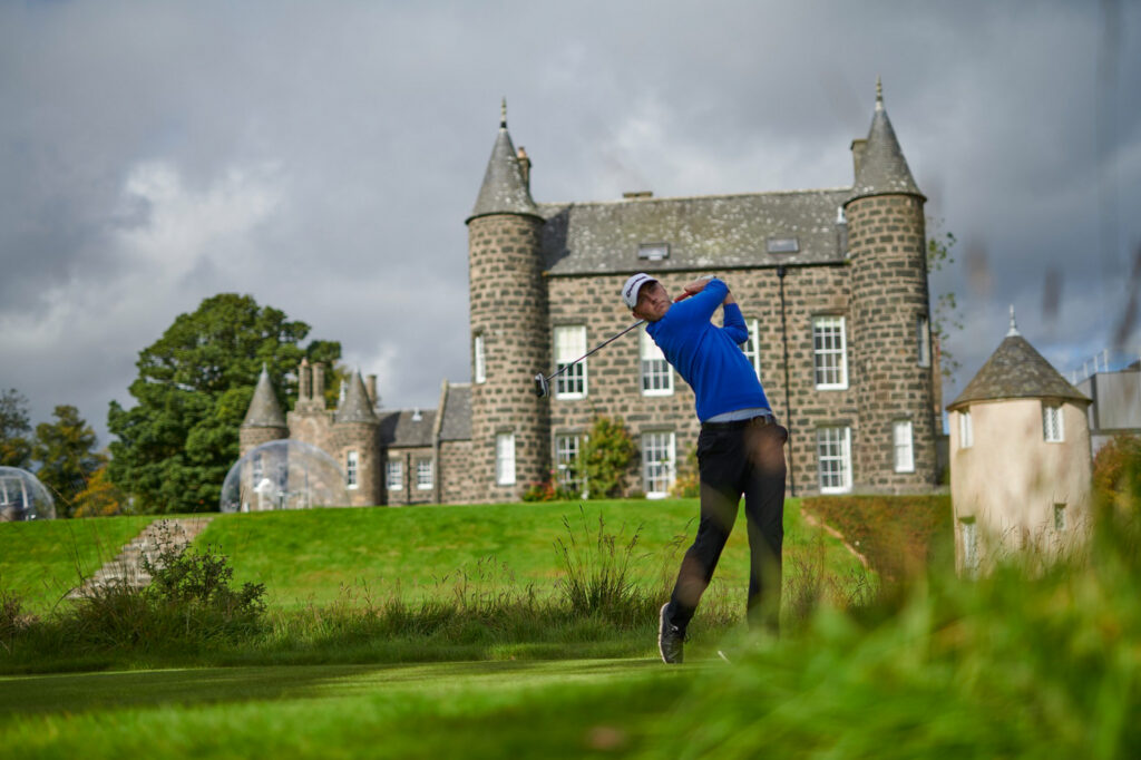 Person playing golf at Meldrum House Golf Club with building in background