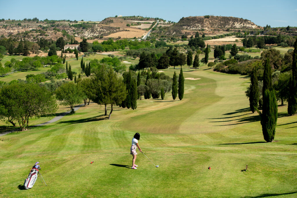 Person playing golf off a tee box at Minthis Golf Club with trees and fairway ahead of her