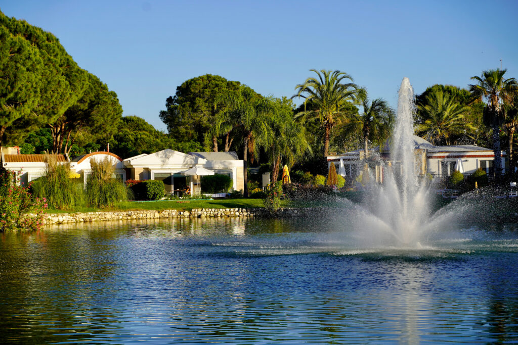 Lake with fountain with trees and building in background at Nobilis Golf Course