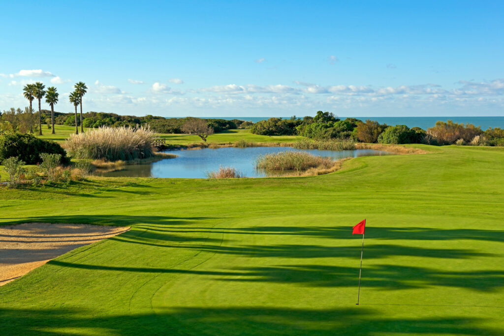 Hole with red flag and lake in the background at Real Novo Sancti Petri Golf Club - B Course