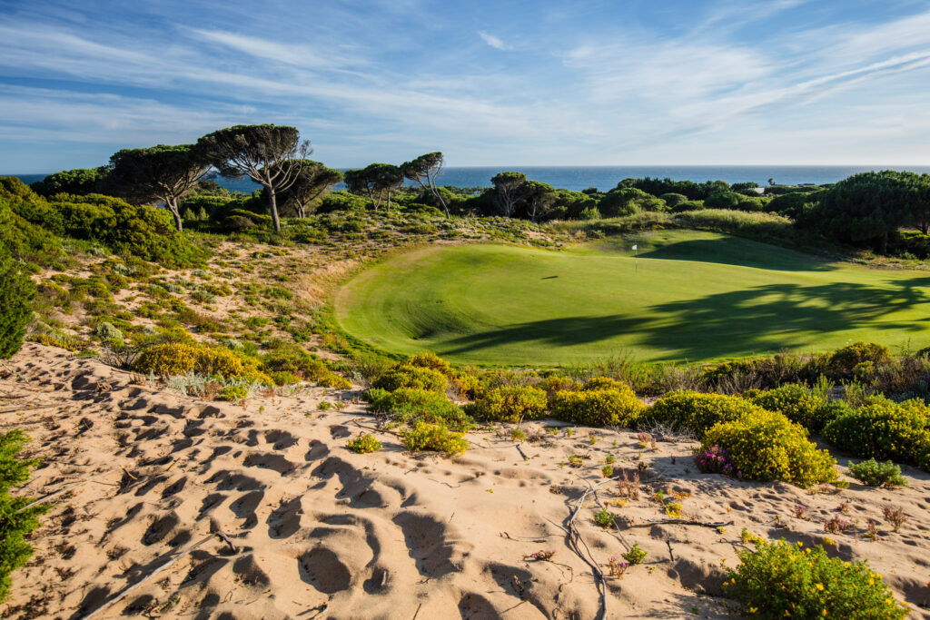 Hole at Oitavos Dunes Golf Course surrounded by trees and sand