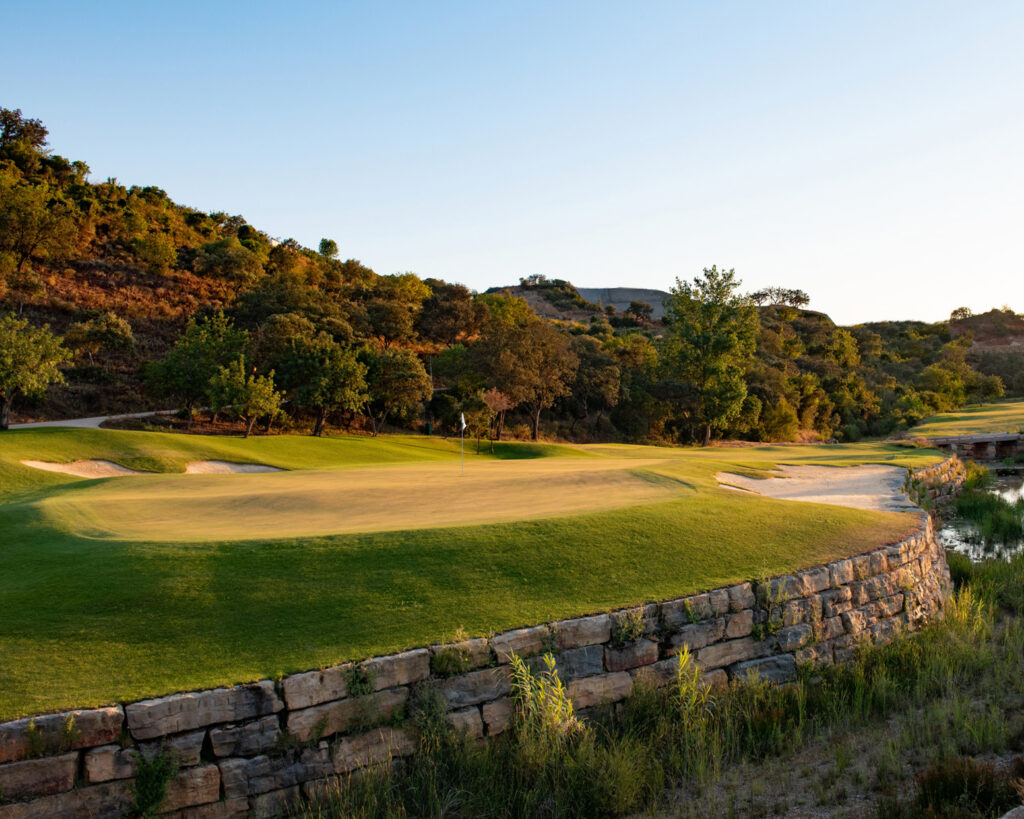 A green with bunkers surrounded by trees and hillsides at Ombria Golf Course