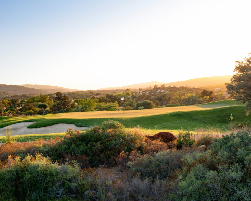 A green with bunker and hills in background at sunset at Ombria Golf Course