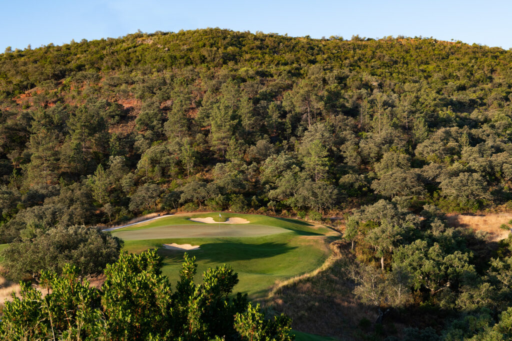 A green with bunkers surrounded by trees on hillside at Ombria Golf Course