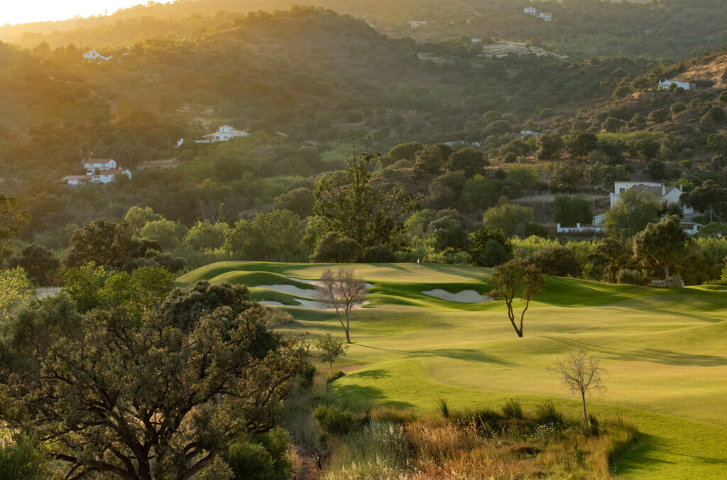 A green with bunkers surrounded by trees and hillsides at Ombria Golf Course