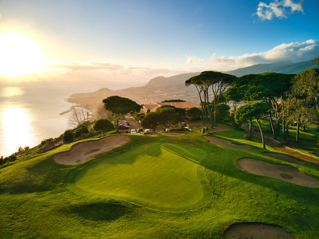 Aerial view of a hole with trees and a lake in the background at Palheiro Golf Course