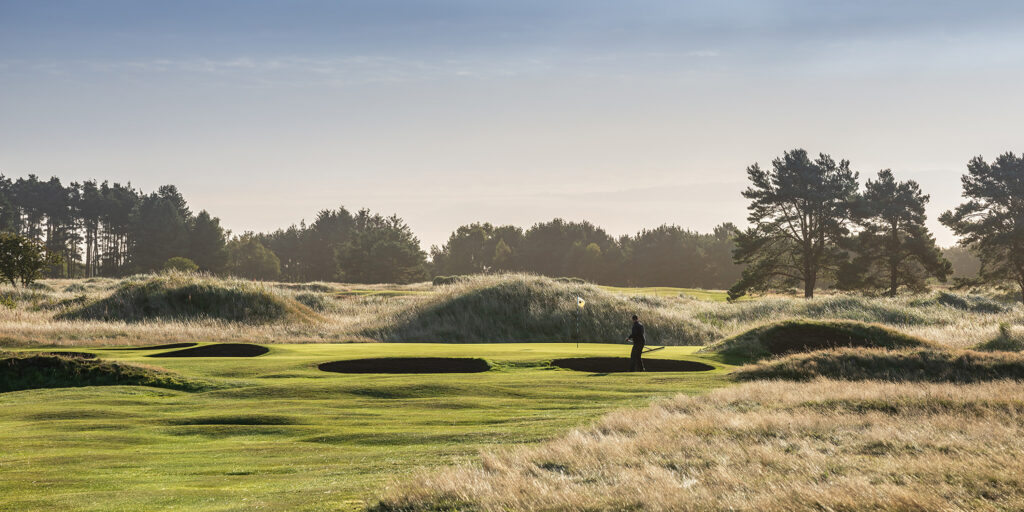 Person raking bunkers at Panmure Golf Club with trees and mound around