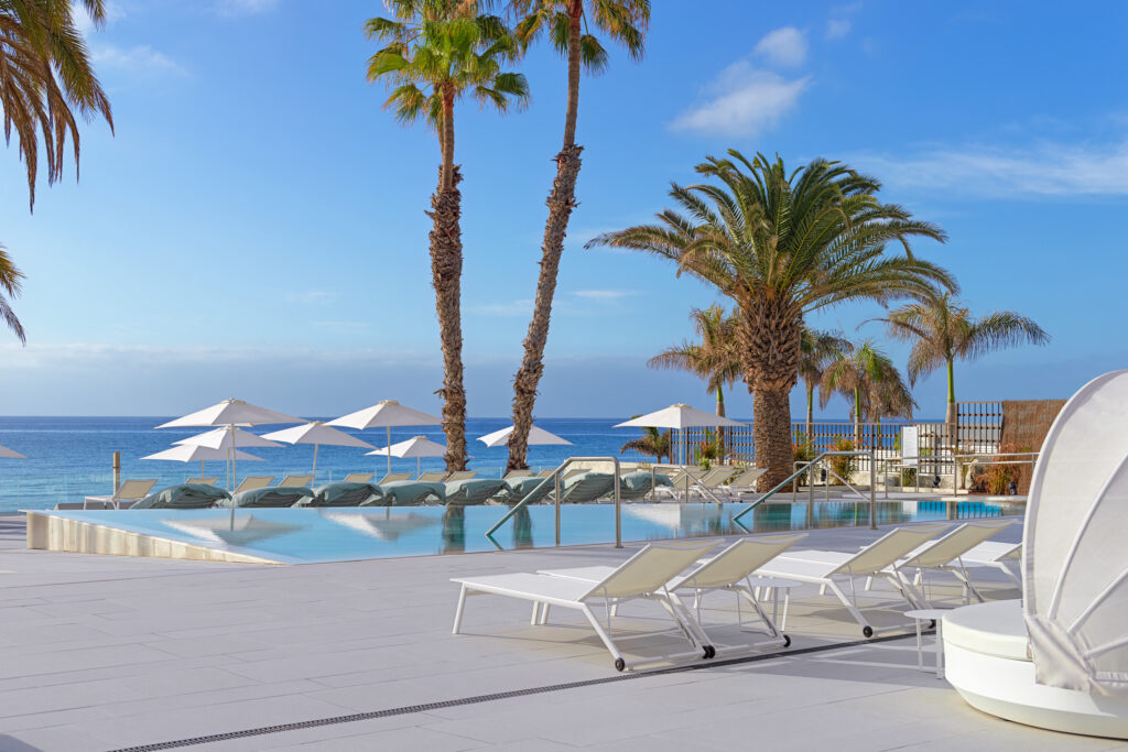 Outdoor pool at Paradisus by Melia Gran Canaria with loungers and palm trees with view of the ocean