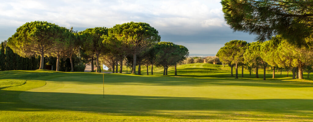 Hole with white flag and trees in background at Peralada Golf Course