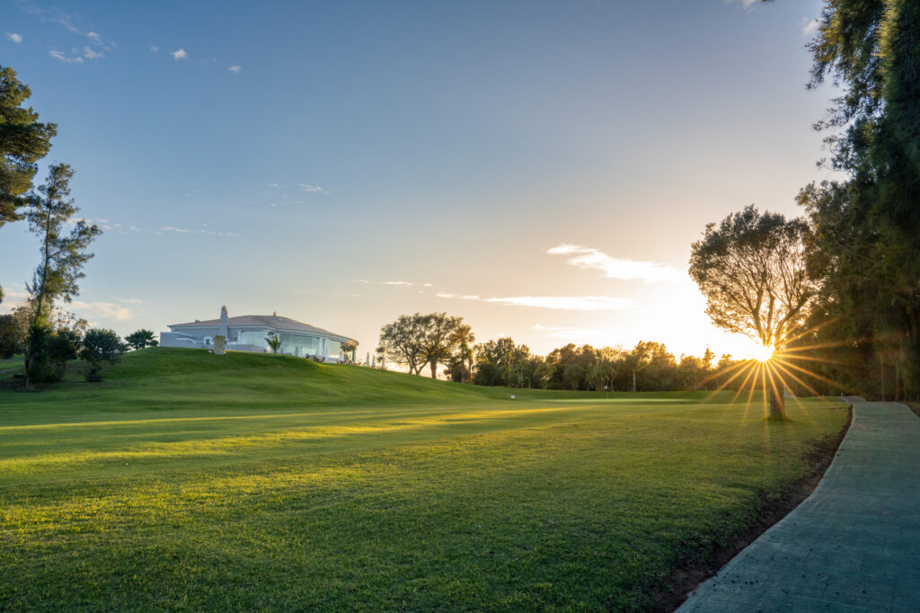 Fairway with building in background and sunset shining through trees at Alto Golf Course