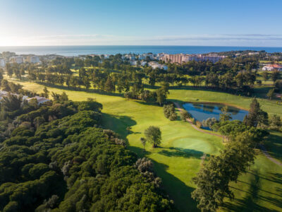 Aerial view of the fairway with water hazard at Alto Golf Course with ocean and buildings in distance