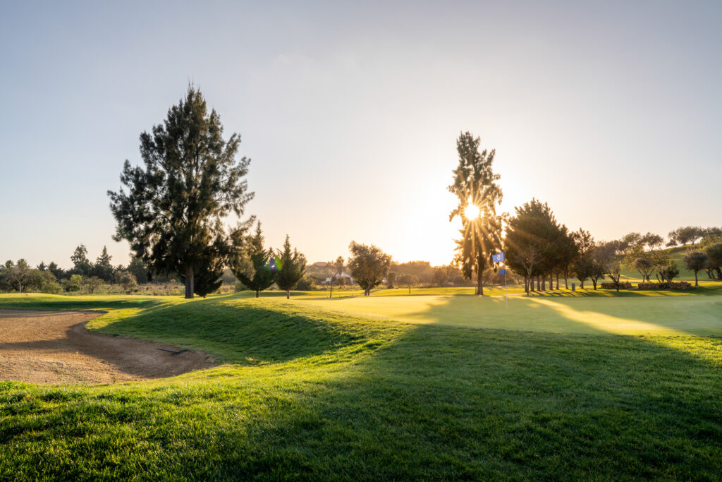 A green with bunker and sun setting through the trees at Silves Golf Course