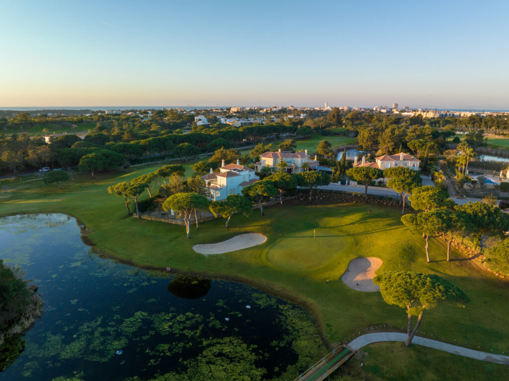 Lake next to a green with bunkers at Vila Sol Golf Course with buildings in background