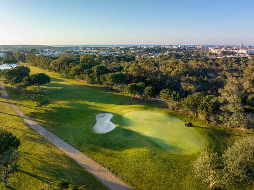 Aerial view of the fairway and a green with a bunker with trees around at Vila Sol Golf Course