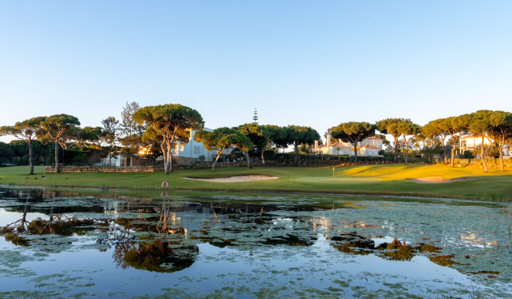 Lake with a green and bunker in background with trees around at Vila Sol Golf Course