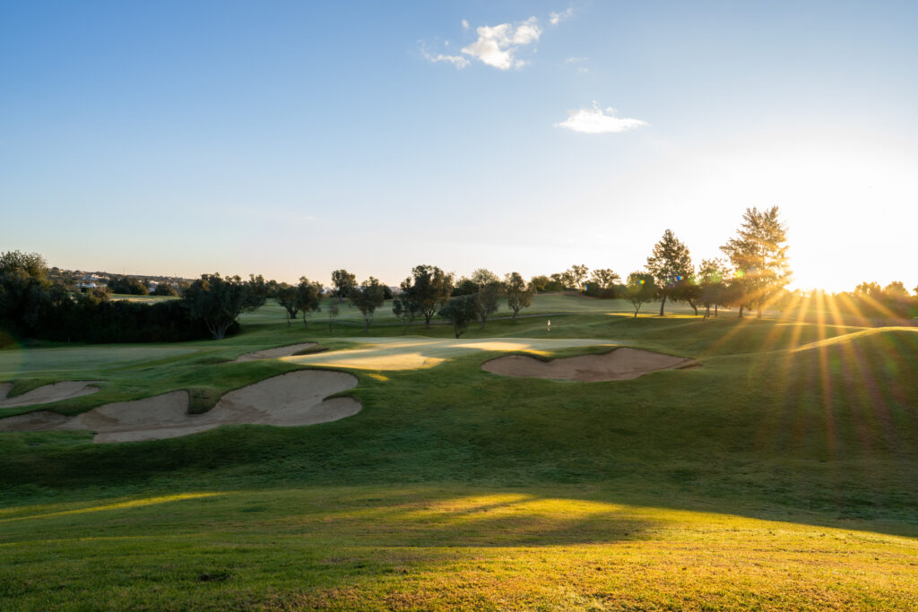 A green with bunkers and sun setting in background at Pinta Golf Course