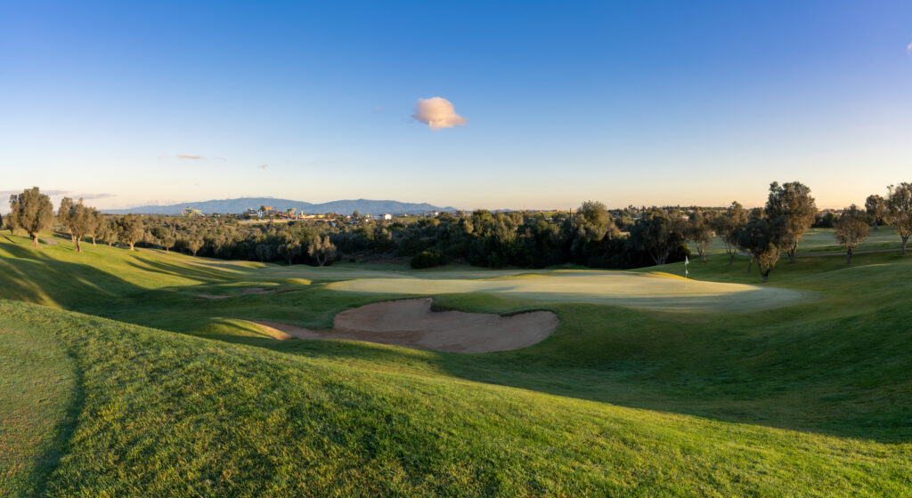 A green with a bunker and trees around at Pinta Golf Course