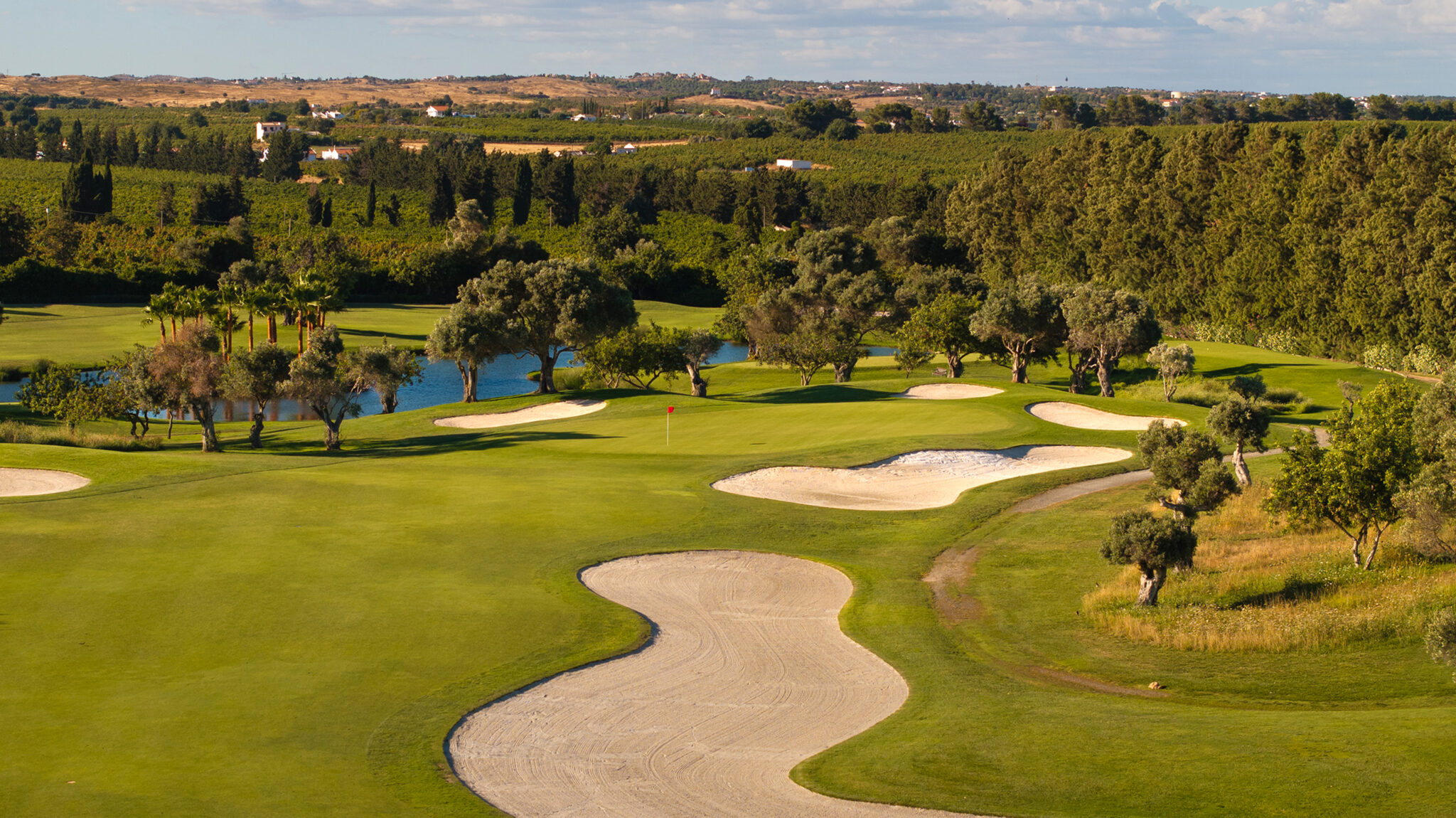 A green with bunkers around it and trees and a lake in the background at Quinta da Ria Golf Course