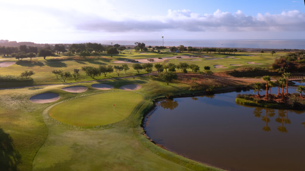 A green with four bunkers around it next to a lake at Quinta da Ria Golf Course