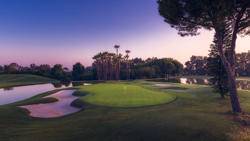 A hole with yellow flag with bunkers and lake and trees around at Real Club Sevilla Golf