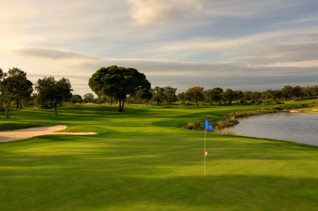 Hole with blue flag with a lake next to it and trees in background at Ribagolfe Lakes Golf Course