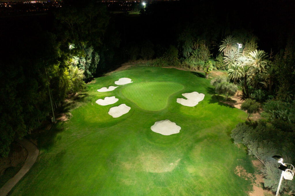 Hole with bunkers at Royal Golf Marrakech at night with trees around