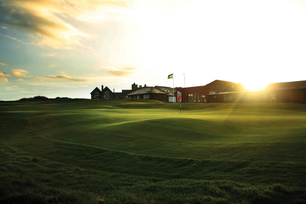 Hole with red flag at Royal Porthcawl with building in background