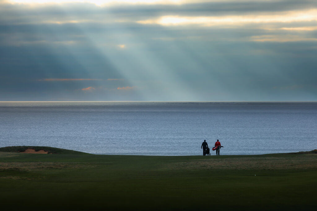 People carrying their bags across Royal Porthcawl with ocean view