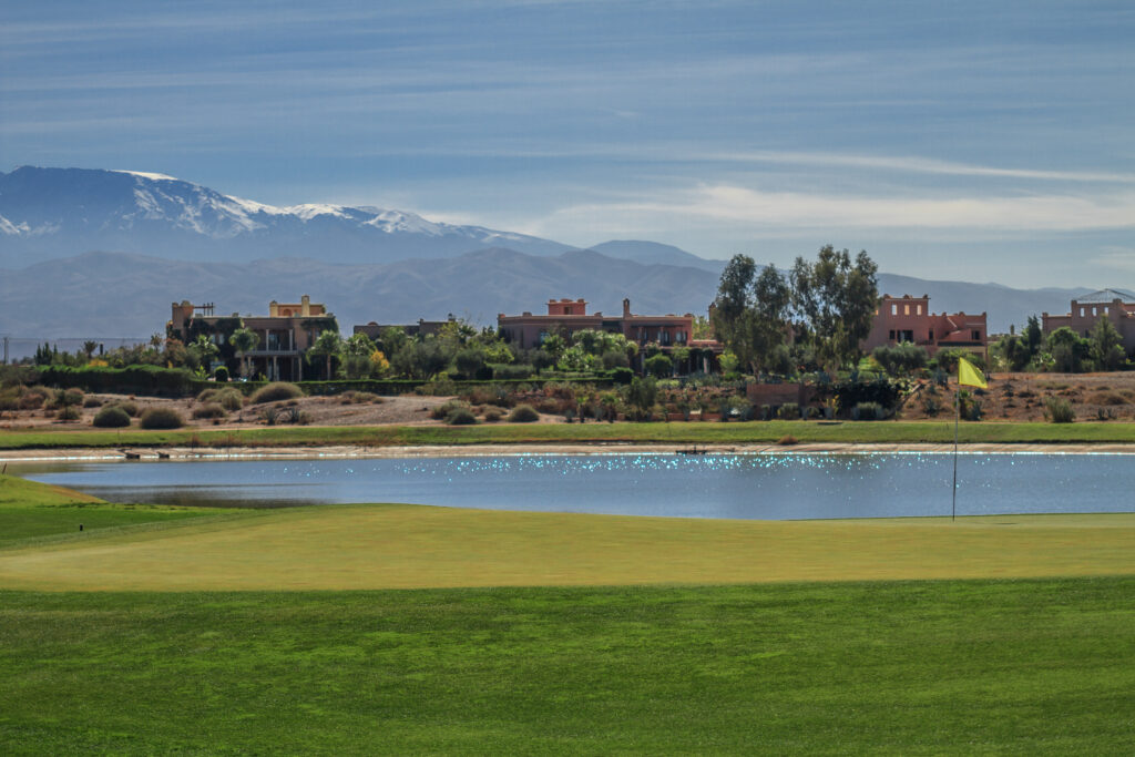 Hole with lake at Samanah Golf & Country Club with buildings and mountains in distance