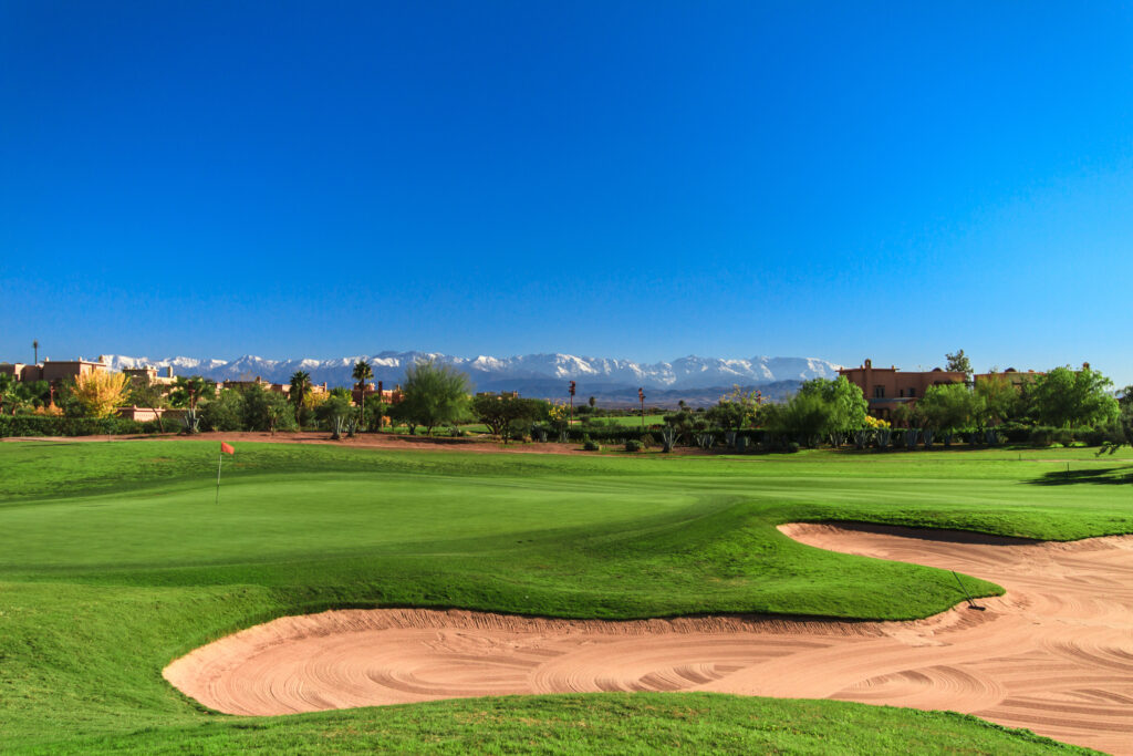 Hole with bunker at Samanah Golf & Country Club with trees and mountains in distance