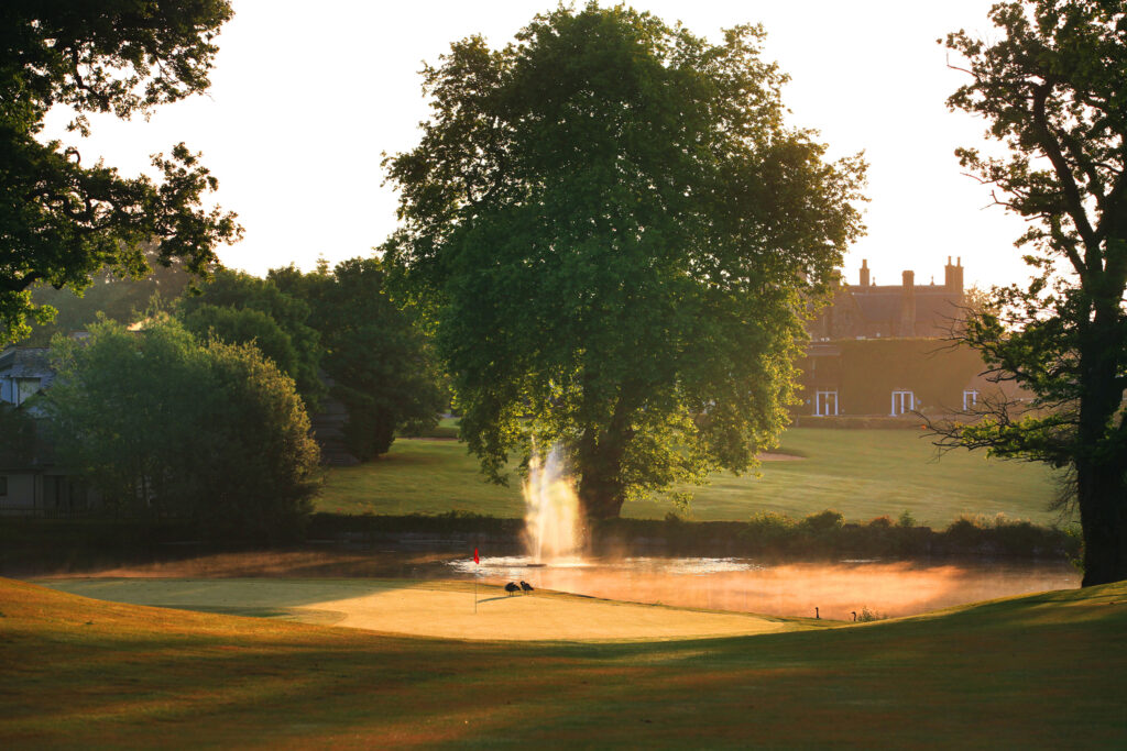 Hole with red flag and water hazard with fountain at St Pierre - Mathern Course with trees around