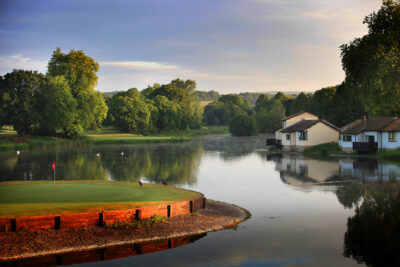 Hole with red flag next to a lake at St Pierre - Mathern Course with buildings and trees around