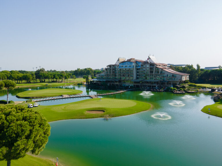 A golf course picture with the club house in the background and a golf hole and lake in the foreground