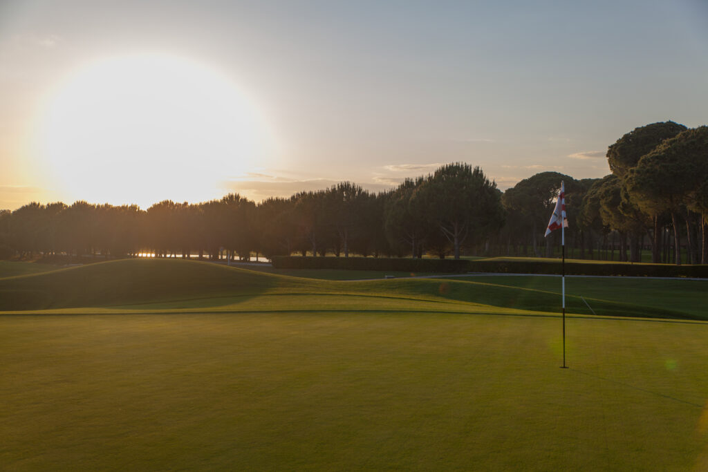 Hole with red and white flag with trees around at PGA Sultan Golf Course