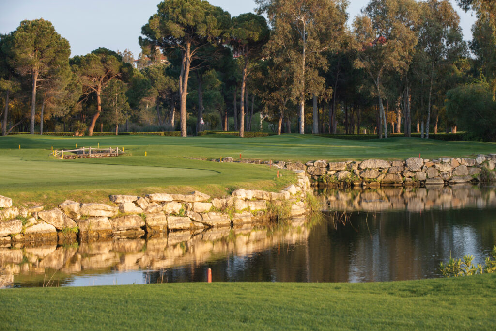 Lake with stone wall with fairway and trees in background at PGA Sultan Golf Course