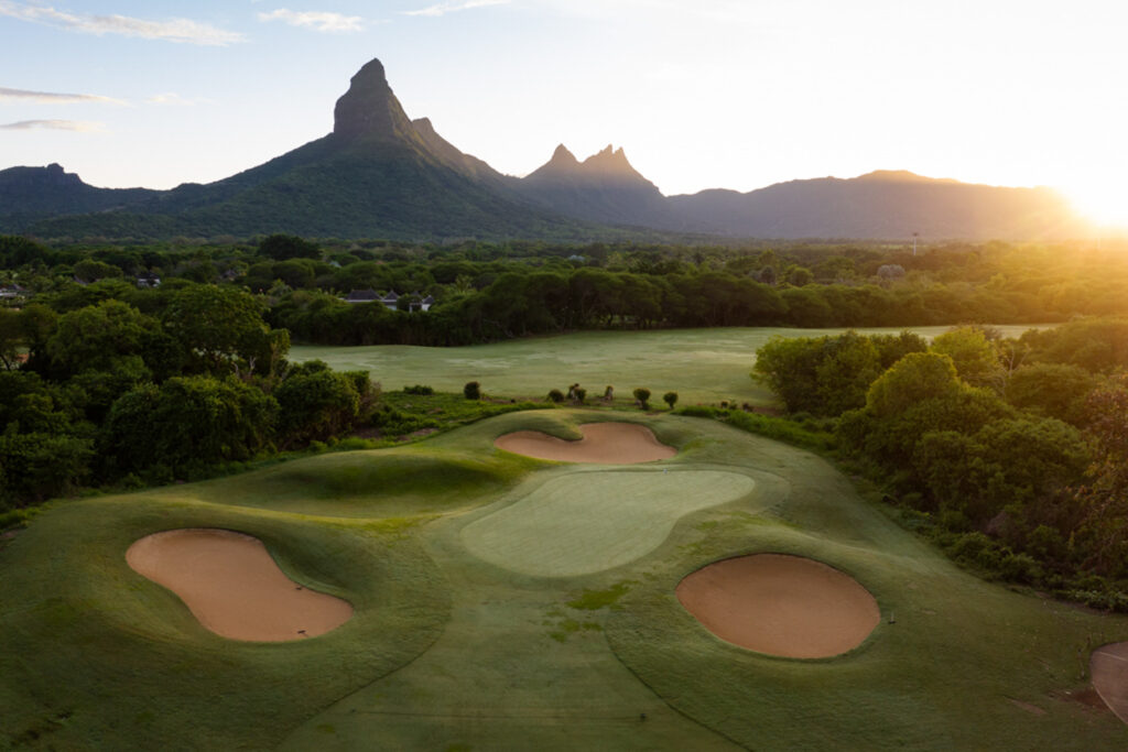 Hole with bunkers at Tamarina Golf Club with trees around and mountain in distance