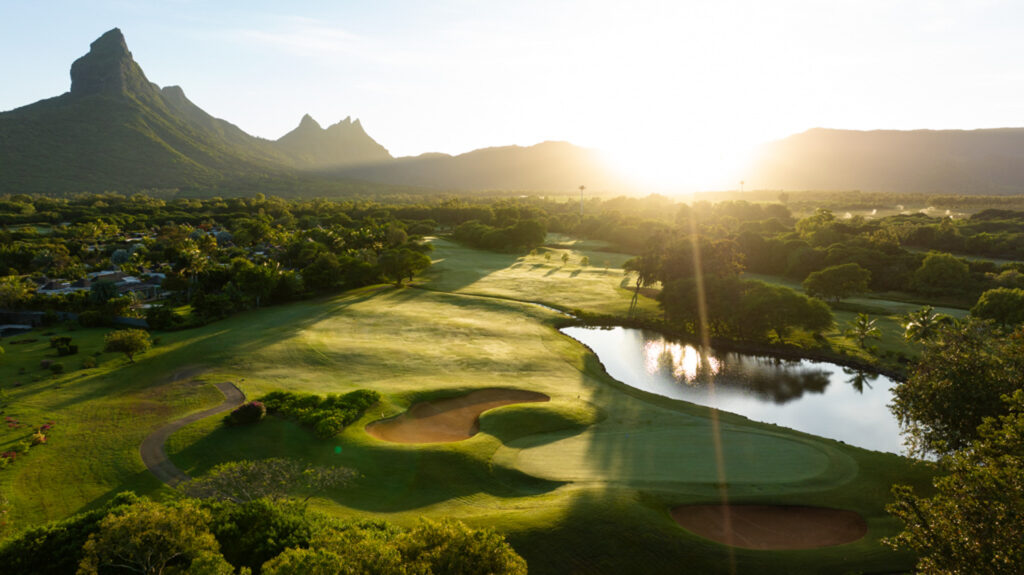 Hole with bunkers at Tamarina Golf Club with trees and a lake around with mountain in distance