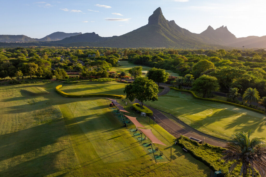 Aerial view of Tamarina Golf Club's driving range with trees around and mountains in distance