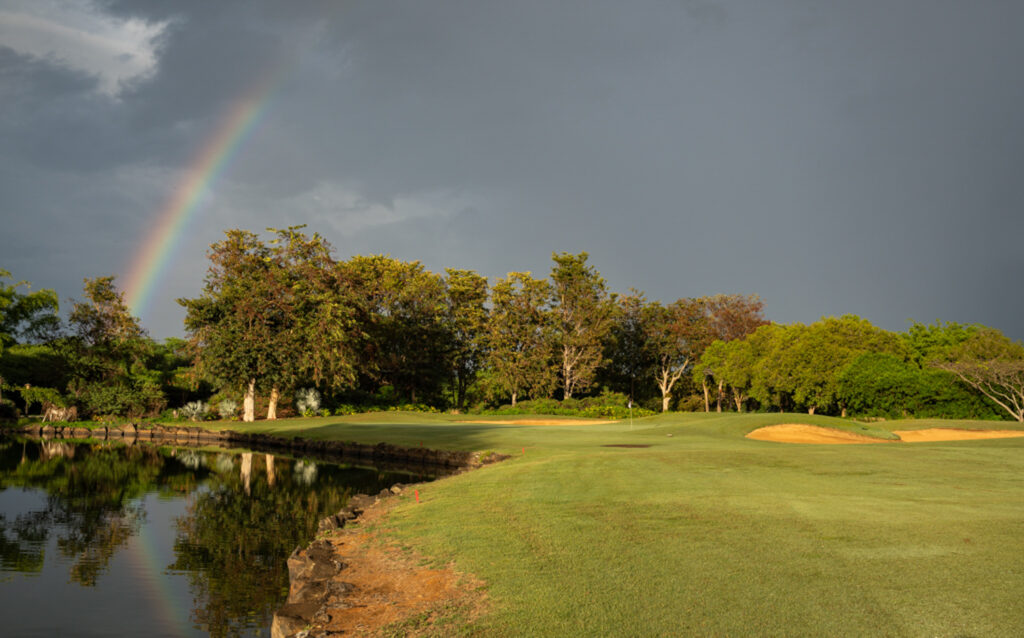 Hole with trees around at Tamarina Golf Club with rainbow in sky