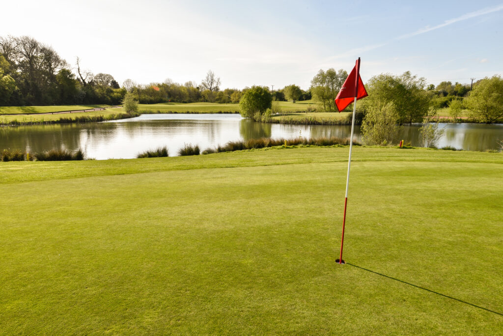 Red flag on hole at The Nottinghamshire Golf & Country Club with lake in background