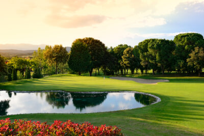 A hole with a white flag with a lake at Torremirona Golf Course