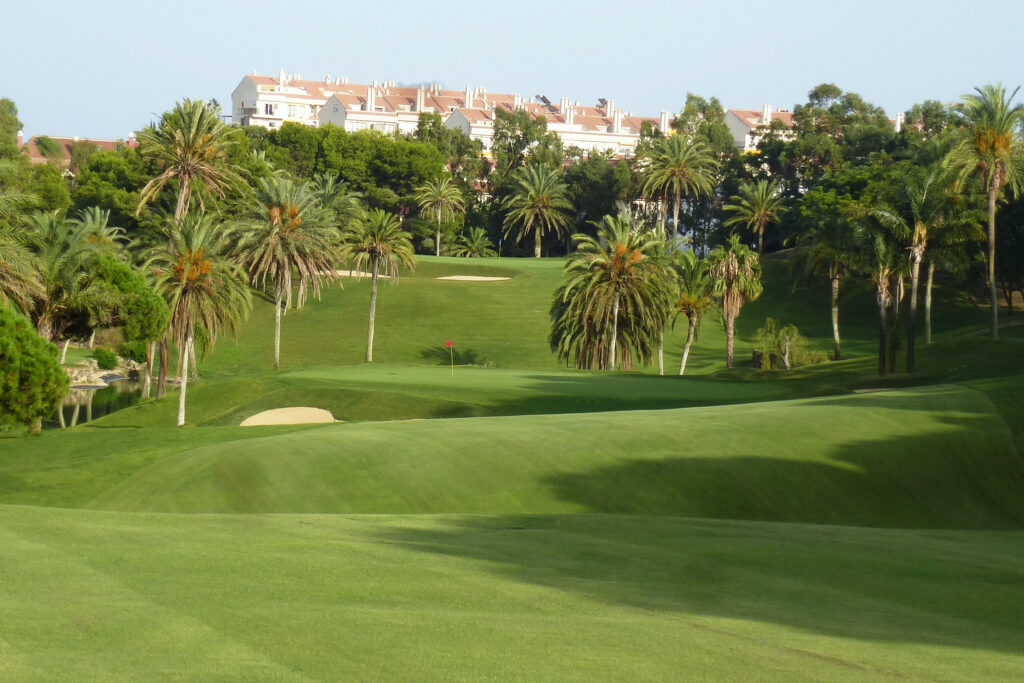 Fairway leading to hole with red flag with trees around at Torrequebrada Golf Course