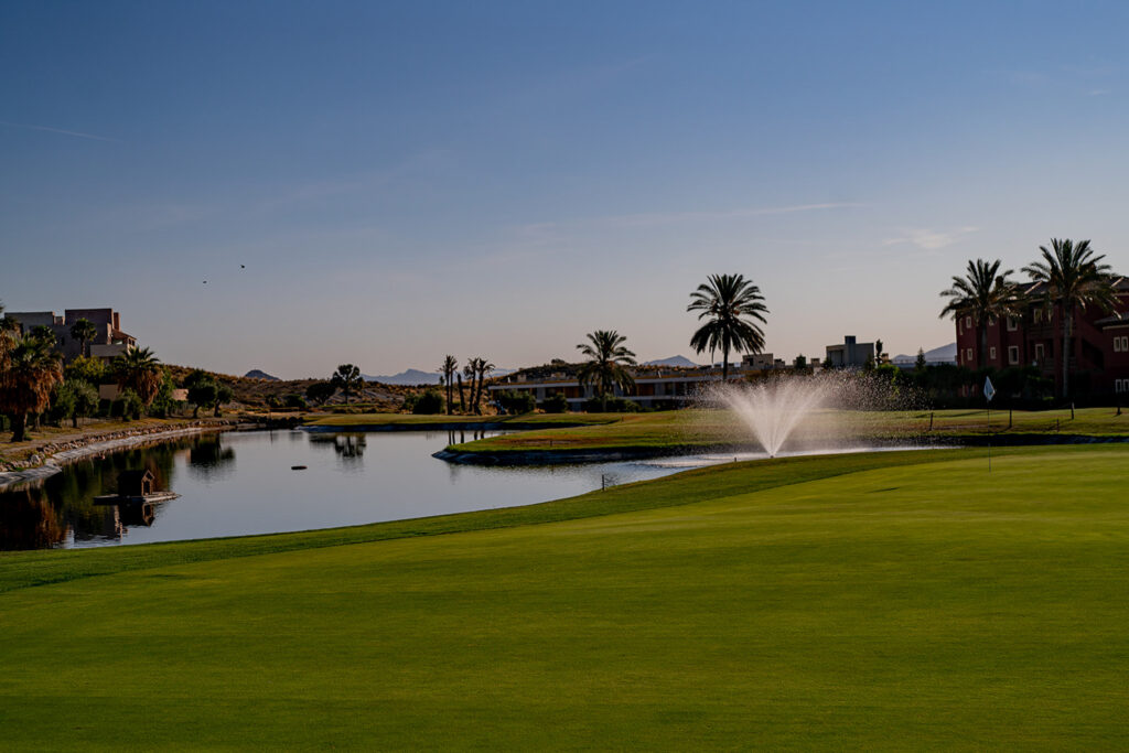 Lake by a green with sprinklers on at Valle Del Este Golf Course