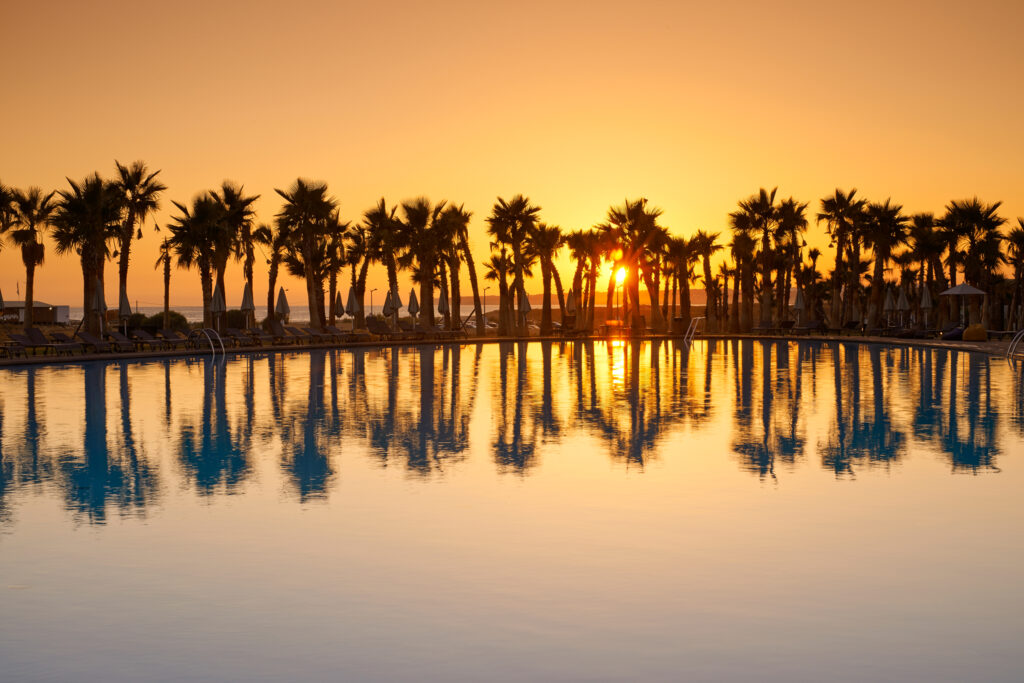 Outdoor pool with palm trees and sun setting in background at Vidamar Resort Hotel Algarve