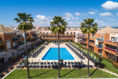 View of outdoor pool with sun loungers and palm trees and Vila Gale Tavira hotel in the background