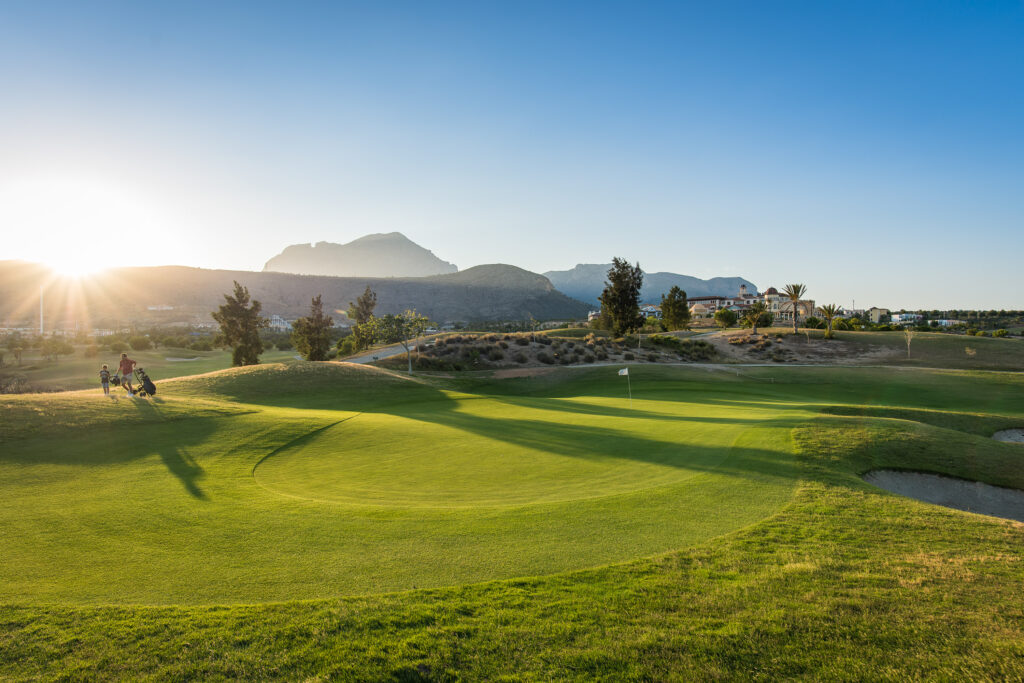 A green with hills in background and sun setting at Villaitana - Levante Course