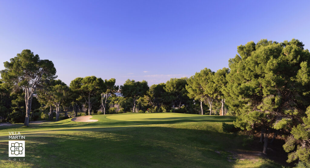 A hole with a red flag at Villamartin Golf Course with trees in the background