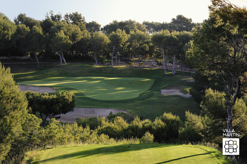 A hole with a red flag at Villamartin Golf Course with trees around and bunkers