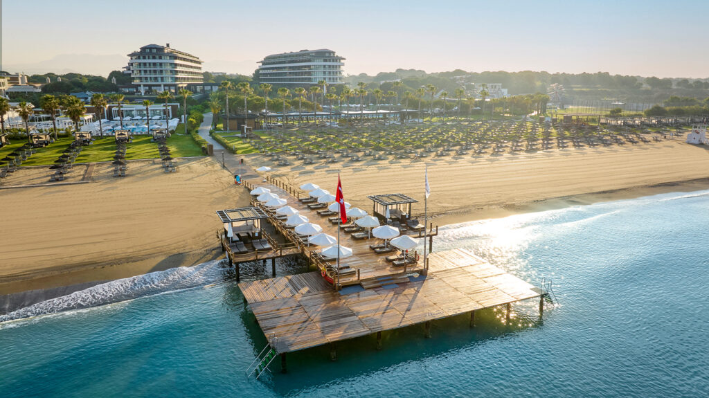 Loungers on beach and deck leading into ocean at Voyage Belek Golf & Spa