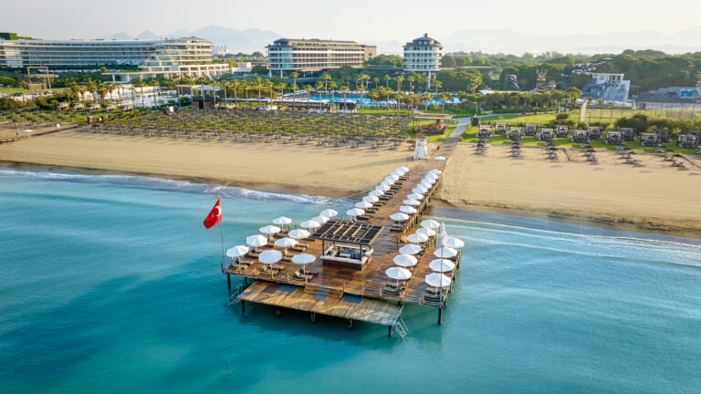 View of the beach with loungers on deck leading into ocean at Voyage Belek Golf & Spa